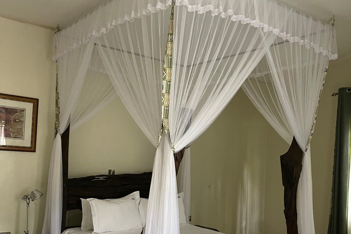 A carved four-poster bed with mosquito net and African-print accents at Maya Nature Resort.