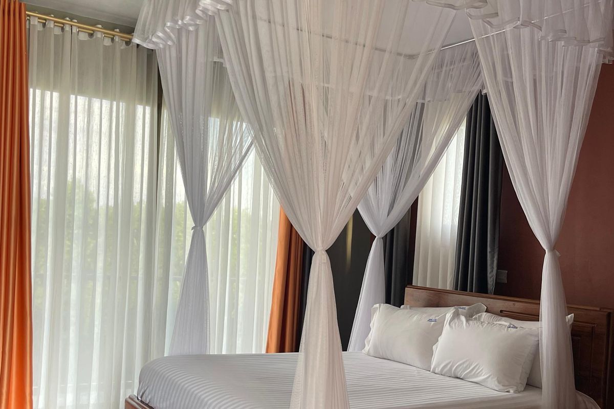 A sunlit four-poster king room with sheer white canopy at Maya Nature Resort.